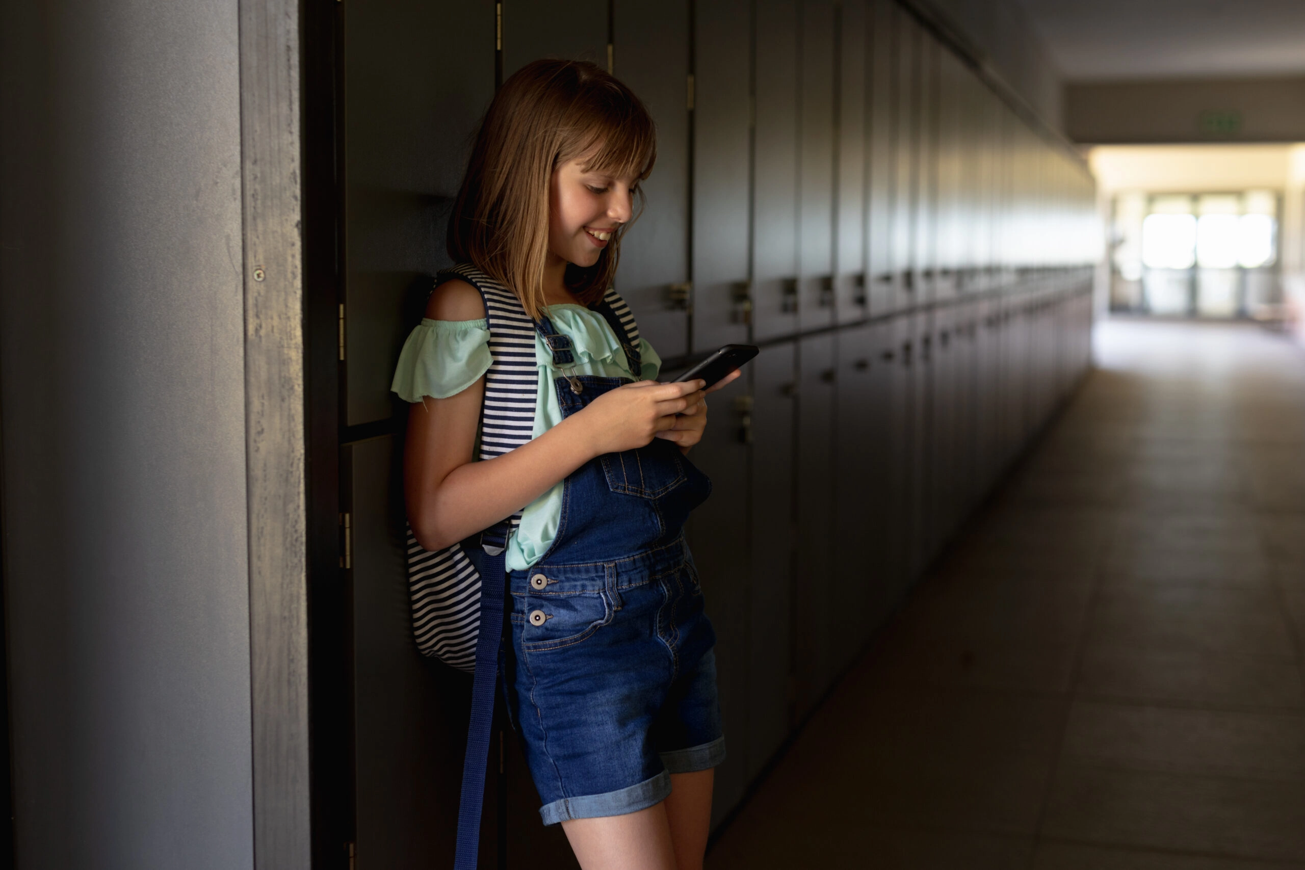 Schoolgirl leaning against lockers in a corridor using a smartphone